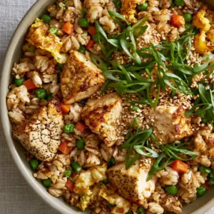 Close-up of soy-glazed jasmine rice grains and seared chicken cubes in a matte bowl. (chicken fried rice)