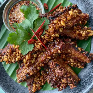 Macro shot of Thai Fried Pork strips showing charred edges and golden garlic clusters on a dark plate. (Thai Fried Pork)