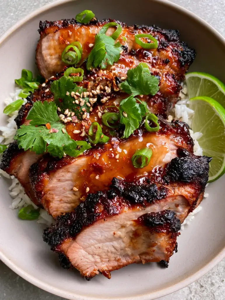 Ginger Lime Pork with Sticky Amber Glaze and Crispy Charred Edges 1 Angled close-up of glistening Ginger Lime Pork slices in a matte bowl with lime wedges and red chili flakes.